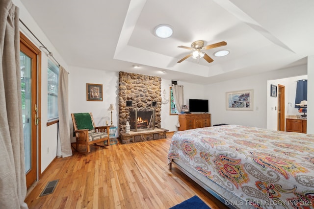 149 SE 4404th Loop, Locust Grove, OK 74352 - bedroom with a raised ceiling, light wood-style flooring, a fireplace, and a ceiling fan