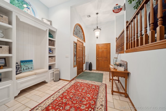 foyer entrance with baseboards, visible vents, light tile patterned floors, and a towering ceiling