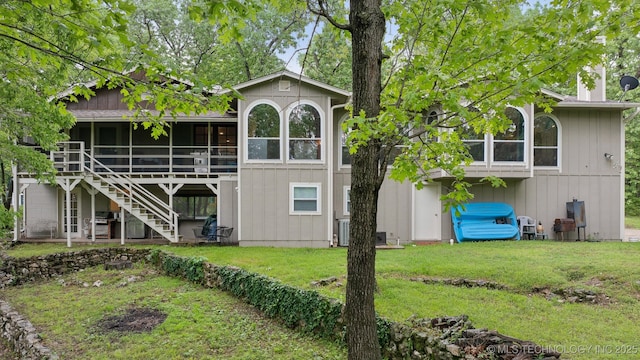 back of property with a lawn, a sunroom, a wooden deck, and stairway