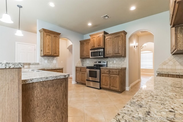 kitchen featuring pendant lighting, tasteful backsplash, arched walkways, light tile patterned floors, and stainless steel appliances
