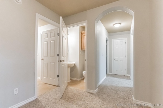 corridor with arched walkways, baseboards, and light carpet