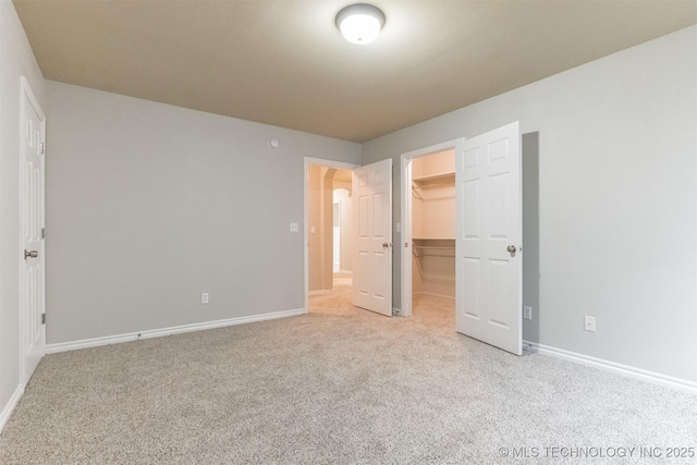unfurnished bedroom with a walk in closet, baseboards, a closet, and light colored carpet