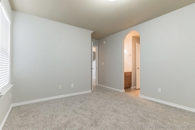 unfurnished room featuring arched walkways, baseboards, and light carpet