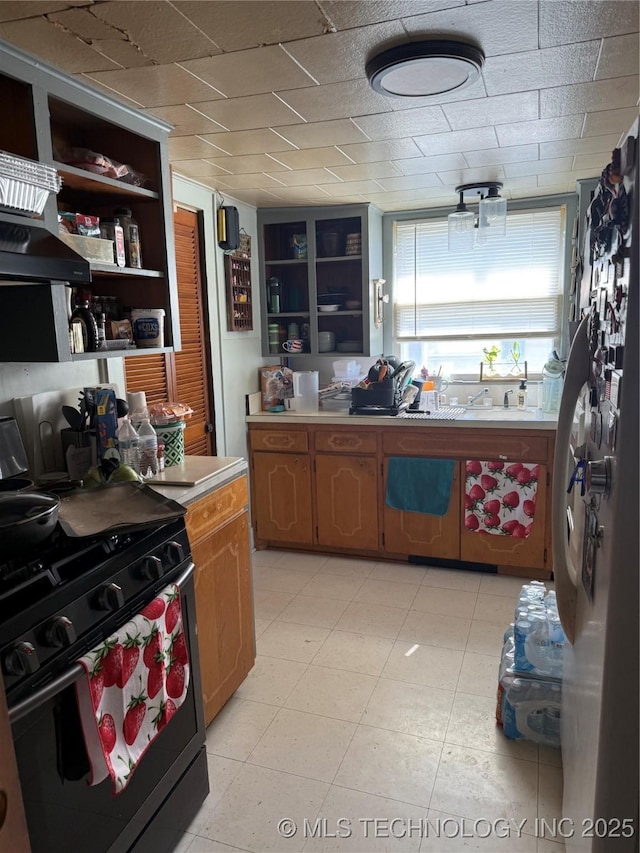 kitchen featuring black gas range, open shelves, light countertops, under cabinet range hood, and a sink