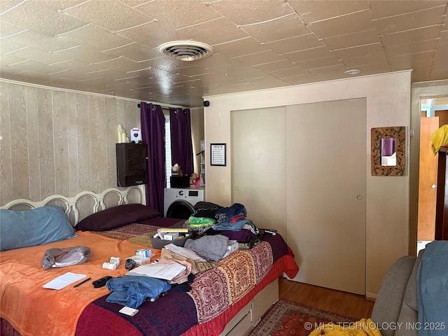 bedroom featuring visible vents, wood walls, washer / dryer, a closet, and wood finished floors