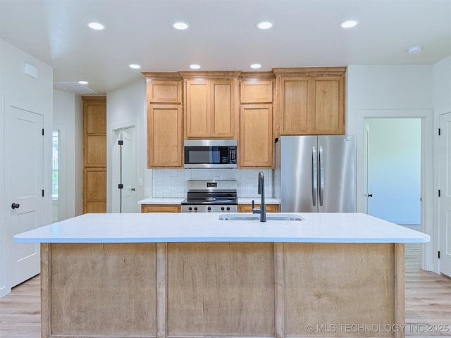 kitchen featuring a sink, light wood finished floors, a kitchen island with sink, stainless steel appliances, and decorative backsplash