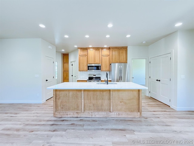 kitchen with appliances with stainless steel finishes, an island with sink, a sink, and light wood-style floors