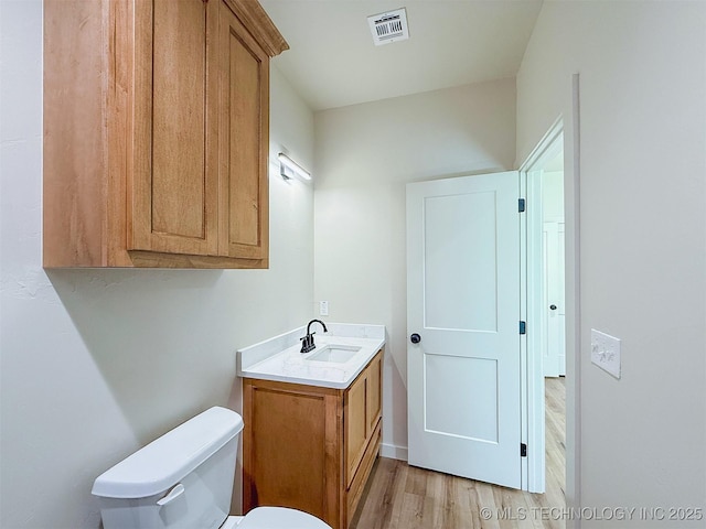 half bathroom with toilet, visible vents, wood finished floors, and vanity