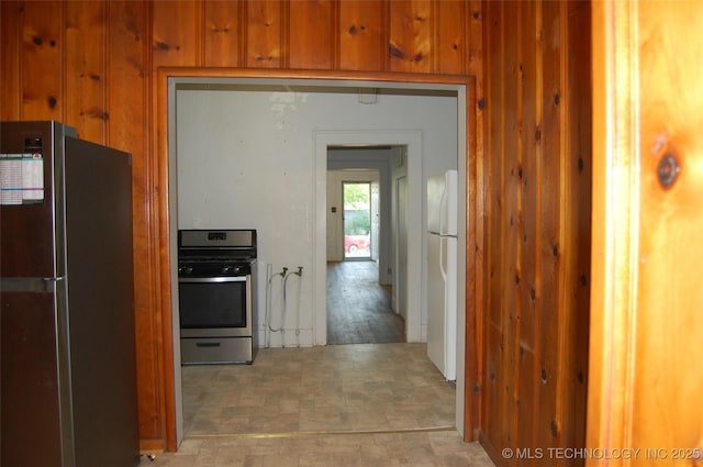 kitchen with freestanding refrigerator, wood walls, brown cabinetry, and gas range