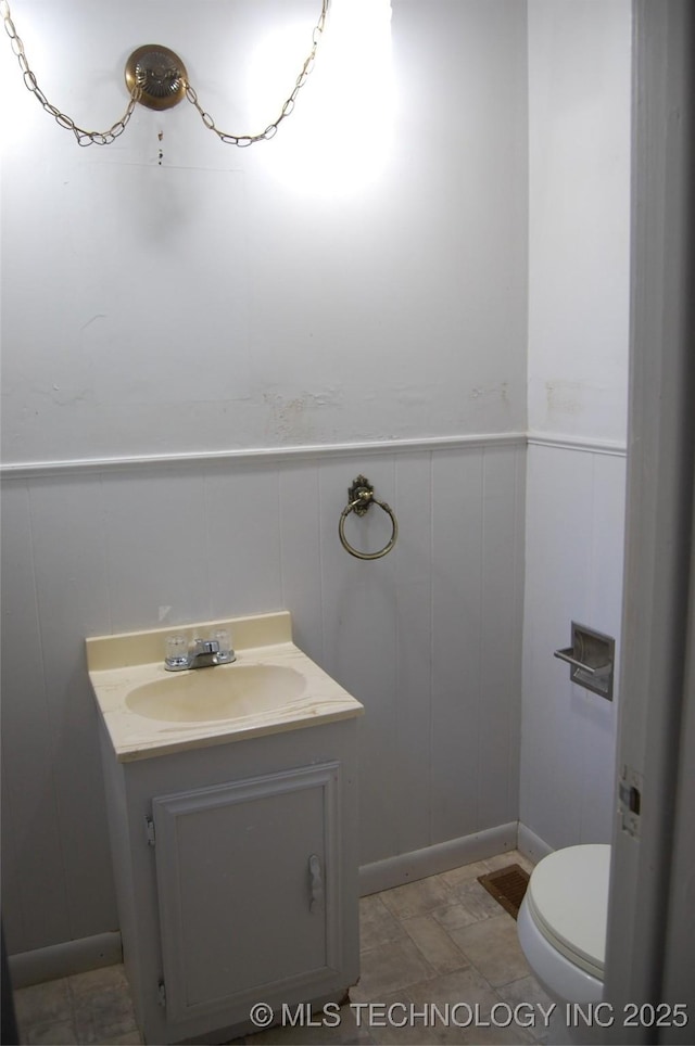 bathroom with vanity, toilet, wainscoting, and a decorative wall