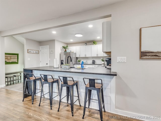 kitchen with white cabinets, a peninsula, dark countertops, and a kitchen bar