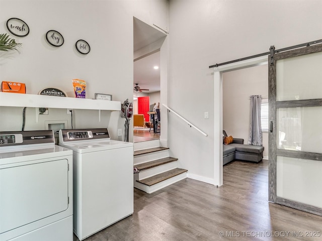 laundry room with laundry area, washing machine and clothes dryer, wood finished floors, a barn door, and baseboards