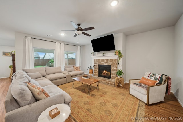 living area with baseboards, a glass covered fireplace, ceiling fan, and wood finished floors