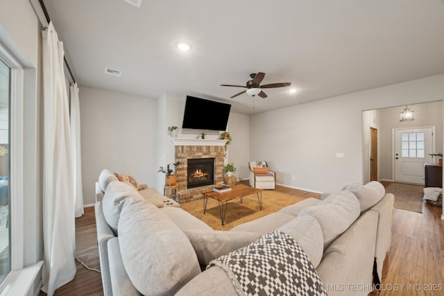 living room with a ceiling fan, visible vents, a fireplace, wood finished floors, and baseboards
