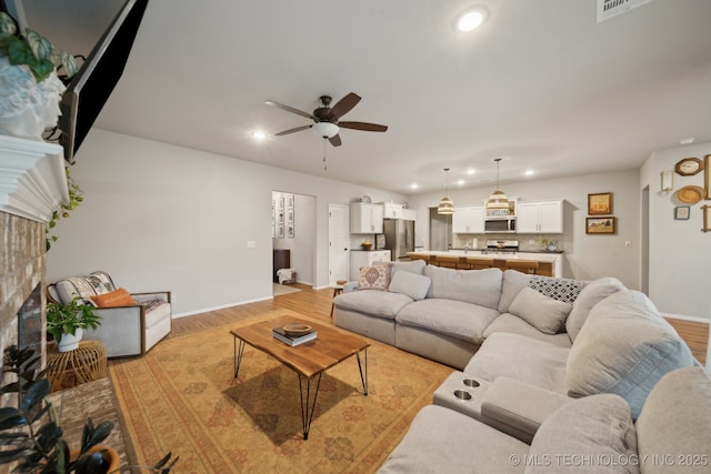 living area featuring a ceiling fan, a fireplace, baseboards, recessed lighting, and light wood-style flooring