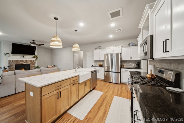 kitchen featuring visible vents, a glass covered fireplace, ceiling fan, a sink, and appliances with stainless steel finishes