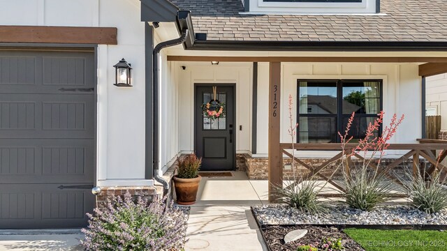 view of exterior entry with covered porch and a shingled roof