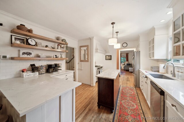kitchen with white cabinets, a sink, light wood finished floors, stainless steel appliances, and decorative backsplash
