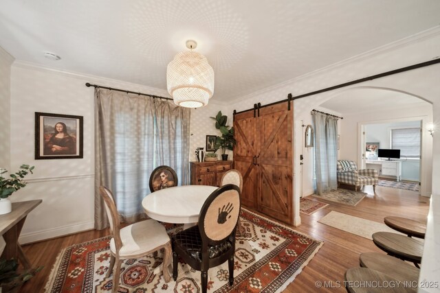 dining room featuring arched walkways, ornamental molding, a barn door, and wood finished floors