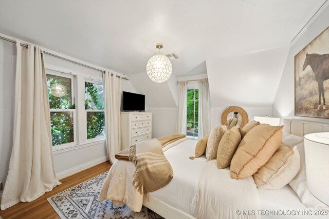 bedroom with baseboards, visible vents, wood finished floors, and lofted ceiling