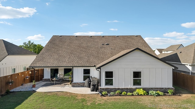 rear view of house with a patio, a fenced backyard, a shingled roof, board and batten siding, and a yard