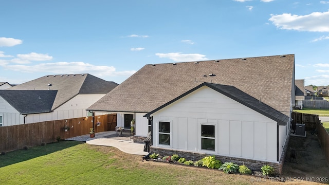 back of house with a lawn, board and batten siding, a shingled roof, and a fenced backyard