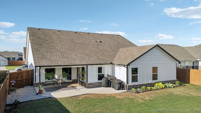 rear view of house with a patio, a fenced backyard, roof with shingles, board and batten siding, and a yard