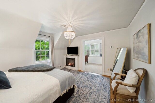 bedroom with visible vents, wood finished floors, baseboards, a warm lit fireplace, and a notable chandelier