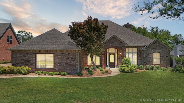 9219 N 134th E Ave, Owasso, OK 74055 - french country style house featuring a shingled roof, a lawn, brick siding, and a chimney