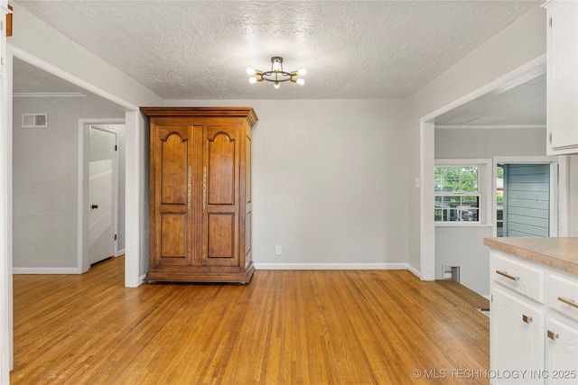 unfurnished room with a textured ceiling, visible vents, light wood-type flooring, baseboards, and a chandelier