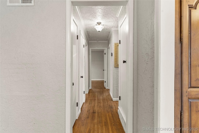 hallway with crown molding, a textured ceiling, a textured wall, and wood finished floors