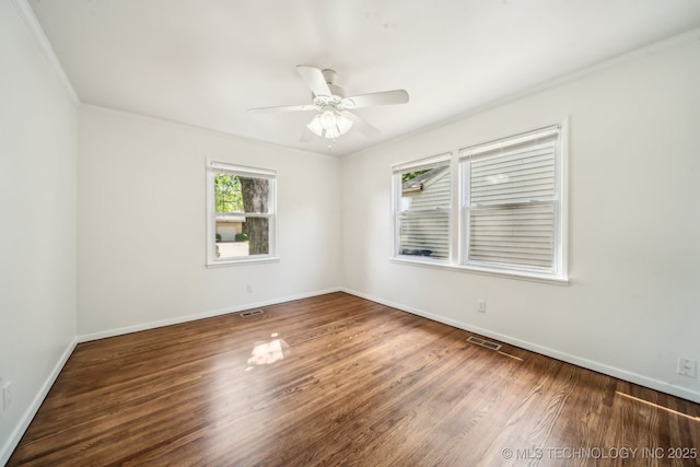 empty room with visible vents, baseboards, crown molding, and wood finished floors
