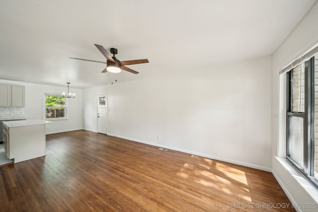 unfurnished living room featuring baseboards, ceiling fan with notable chandelier, and dark wood-type flooring
