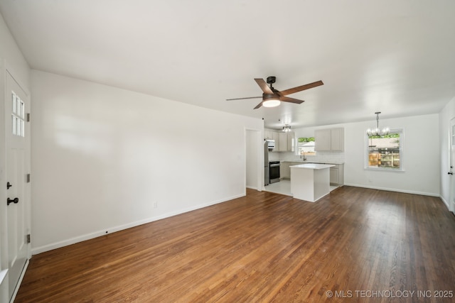 unfurnished living room with a sink, baseboards, ceiling fan with notable chandelier, and dark wood-type flooring