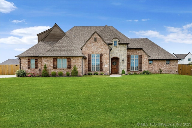 french provincial home with brick siding, a front yard, fence, and roof with shingles