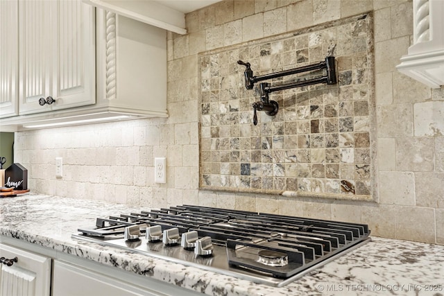 kitchen with light stone counters, white cabinetry, backsplash, and stainless steel gas stovetop