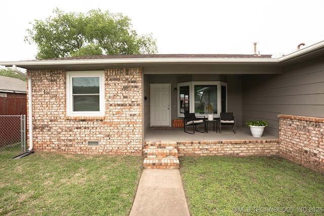 view of exterior entry featuring fence, a lawn, a porch, and brick siding