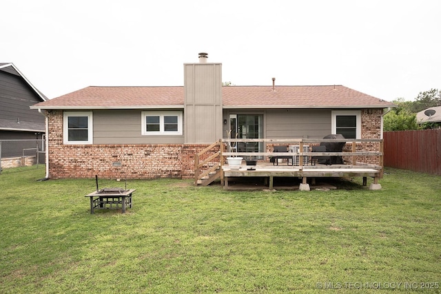 back of property featuring a chimney, a wooden deck, a fenced backyard, a yard, and a fire pit