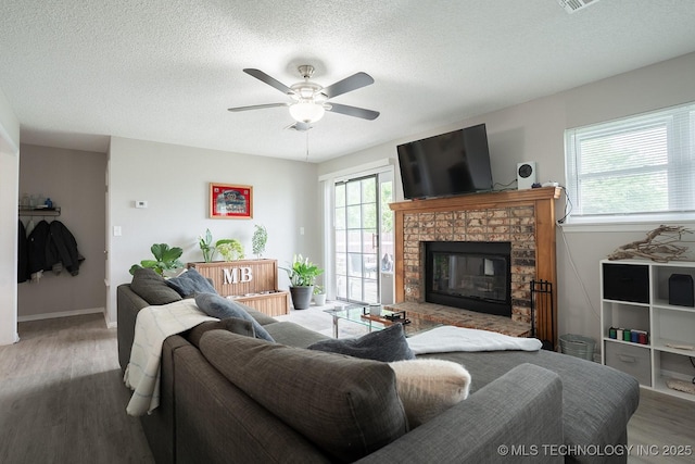 living area featuring a textured ceiling, ceiling fan, wood finished floors, and a fireplace