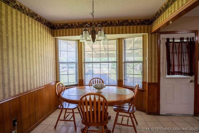 dining room with light tile patterned floors, a wainscoted wall, an inviting chandelier, and wallpapered walls
