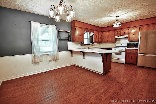 kitchen with a chandelier, stainless steel appliances, a peninsula, under cabinet range hood, and visible vents