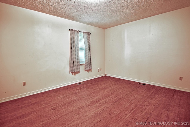 spare room with a textured ceiling, baseboards, wood finished floors, and visible vents