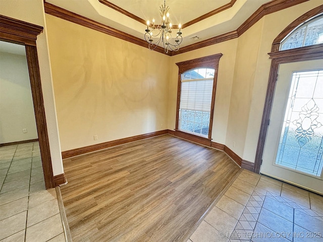 foyer entrance with a chandelier, a tray ceiling, ornamental molding, baseboards, and light wood-style flooring
