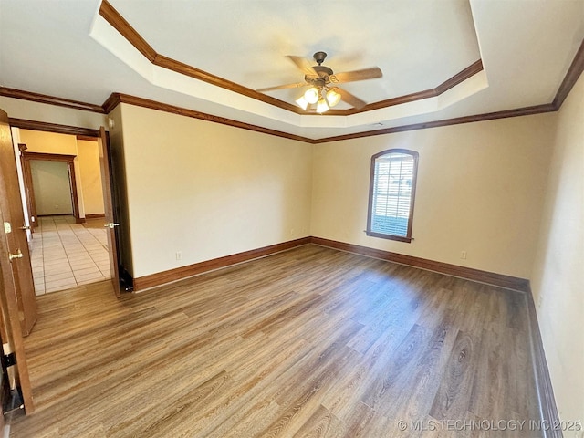 empty room with a tray ceiling, ceiling fan, wood finished floors, crown molding, and baseboards