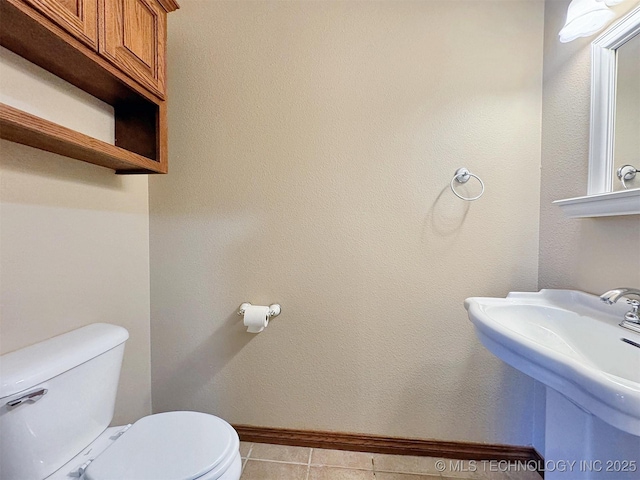 bathroom featuring a sink, baseboards, toilet, and tile patterned flooring