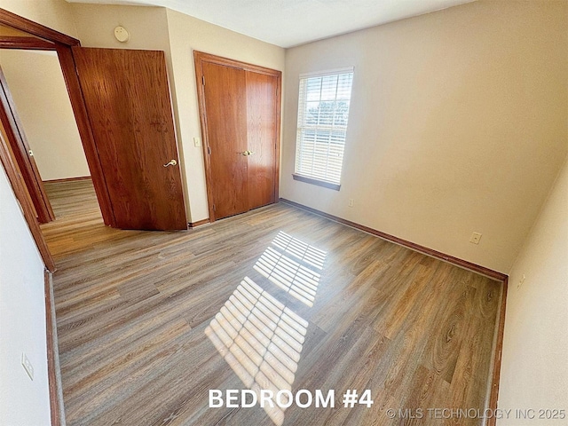 unfurnished bedroom with wood finished floors, baseboards, and a closet