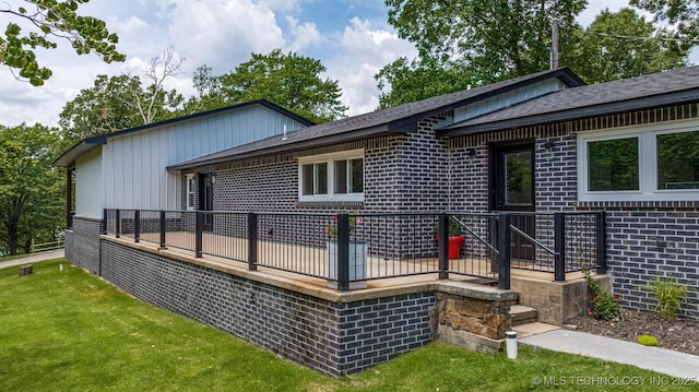 rear view of house featuring brick siding, a lawn, and a wooden deck