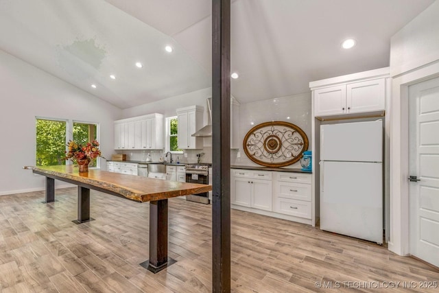 kitchen with appliances with stainless steel finishes, white cabinetry, a sink, high vaulted ceiling, and wall chimney exhaust hood