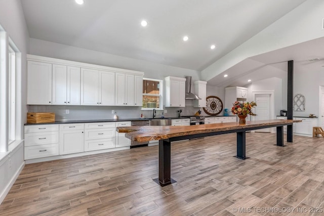 kitchen with wall chimney range hood, dark countertops, light wood-style floors, dishwasher, and white cabinetry
