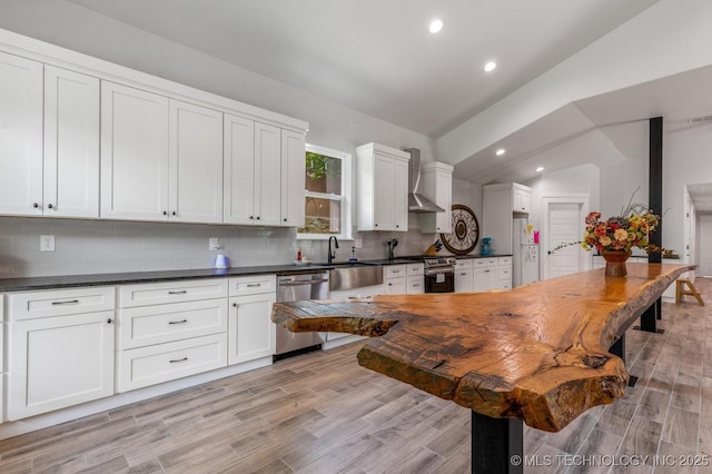 kitchen with appliances with stainless steel finishes, tasteful backsplash, dark countertops, a sink, and wall chimney exhaust hood